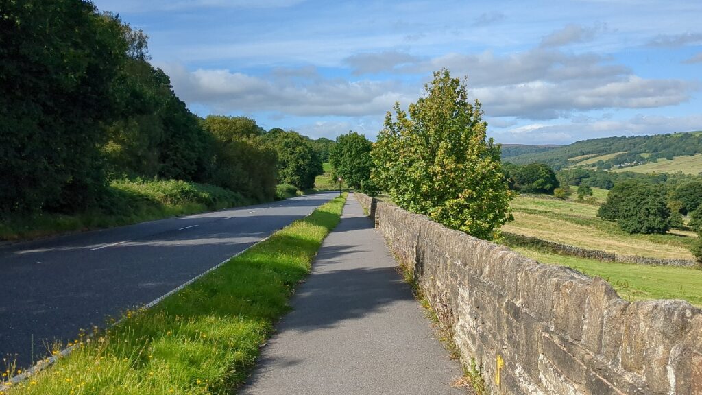 View downhill of a footpath next to a road and a field landscape